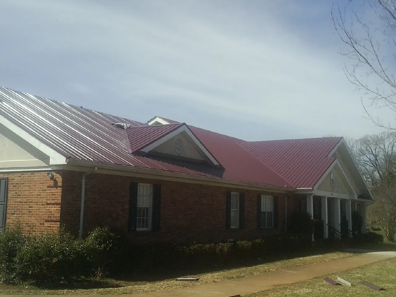 Red metal roof with gabled entries on a long brick building, from a Hail Damage Roof Repair job in El Centro